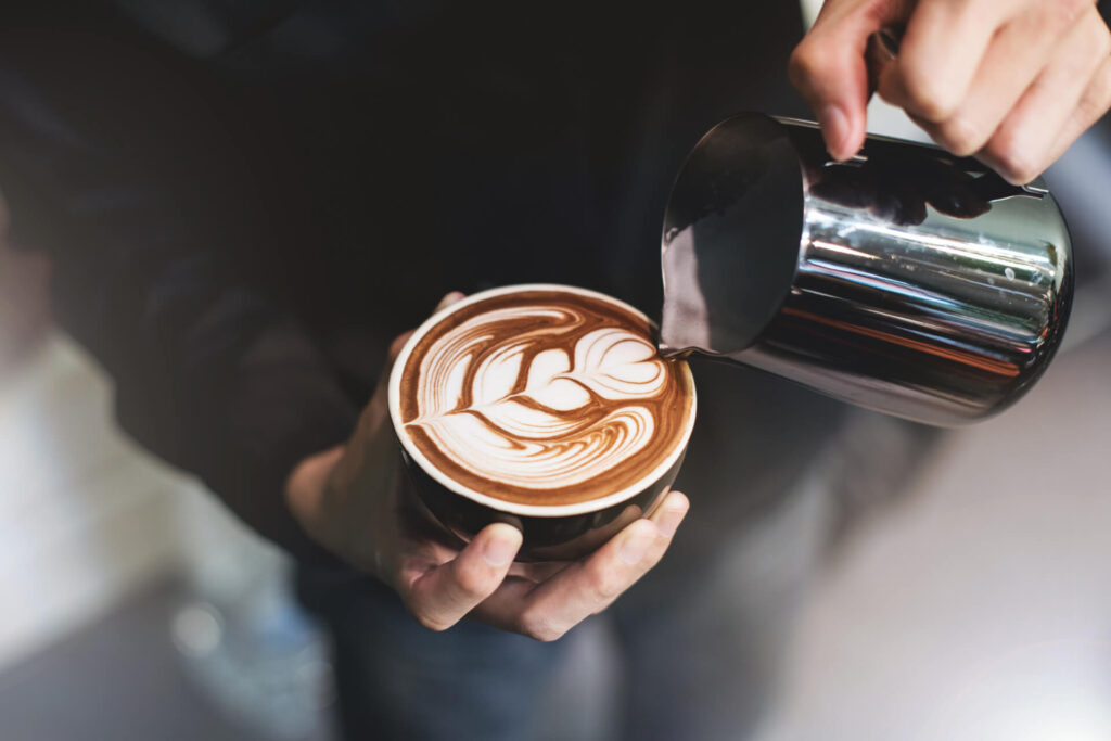 Barista pouring steamed milk to create latte art in a fresh cup of coffee