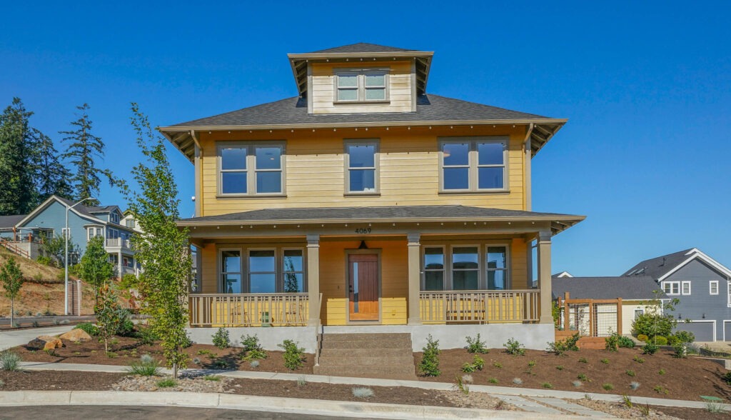 Two-story yellow Craftsman custom home with wraparound porch, tower dormer and new landscaping